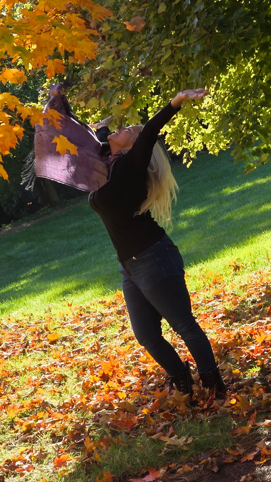 Misti Spencer reaching skyward beneath a tree of turning autumn leaves